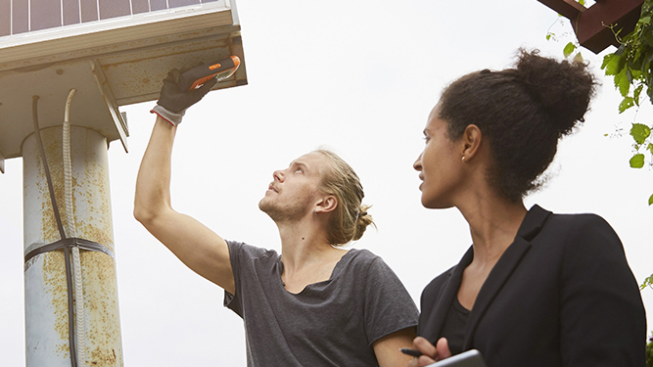 Low angle view of garden architect adjusting solar panel by colleague holding tablet computer